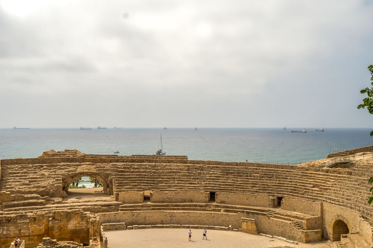 Gradas del anfiteatro romano frente al mar, con barcos en el horizonte.