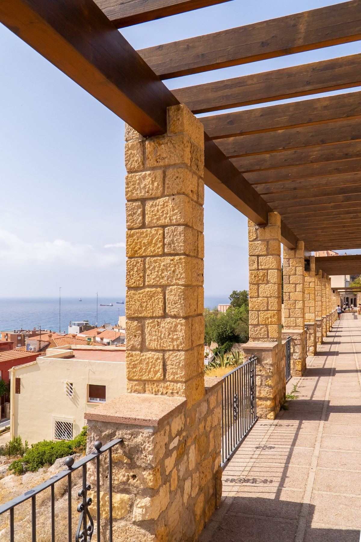 Porches de piedra y madera del passeig arqueològic con vistas al mar.