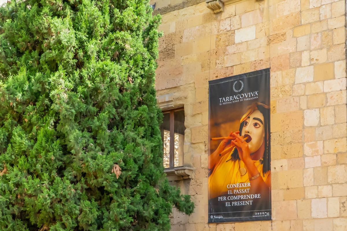 Cartel del festival Tarraco Viva sobre un muro de sillares del casco antiguo.