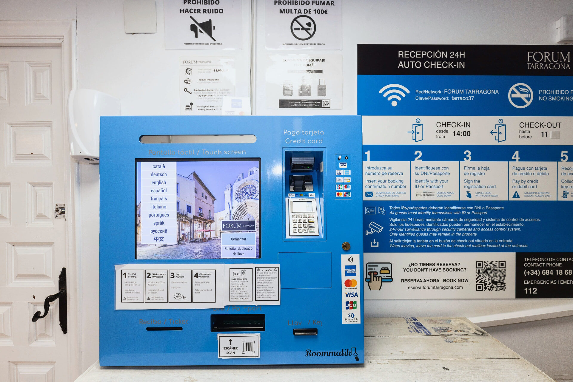 Máquina de auto check-in con pantalla táctil e instrucciones en la recepción del hostal.