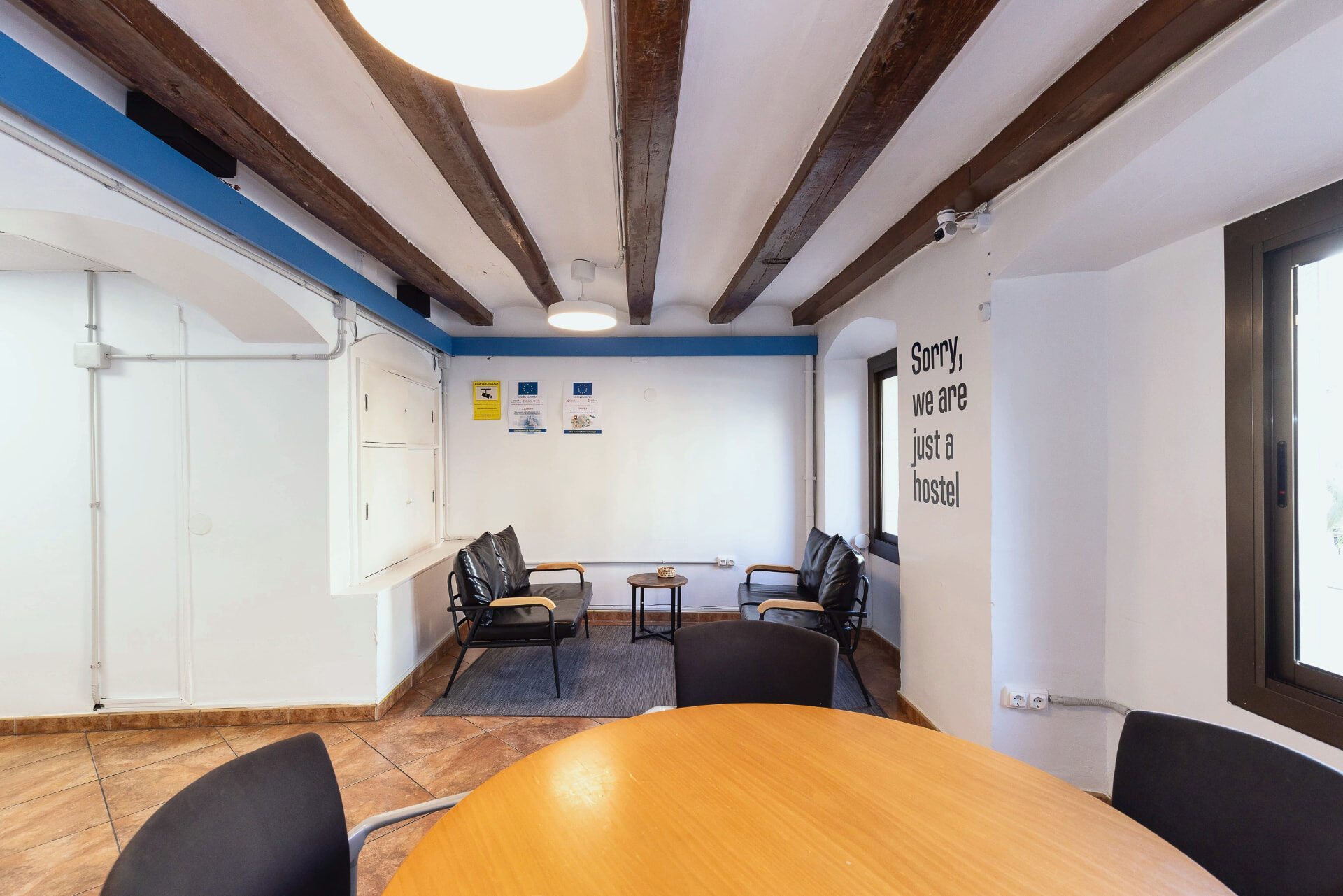 Sala común del hostal con vigas de madera originales, butacas de piel y mesa redonda.