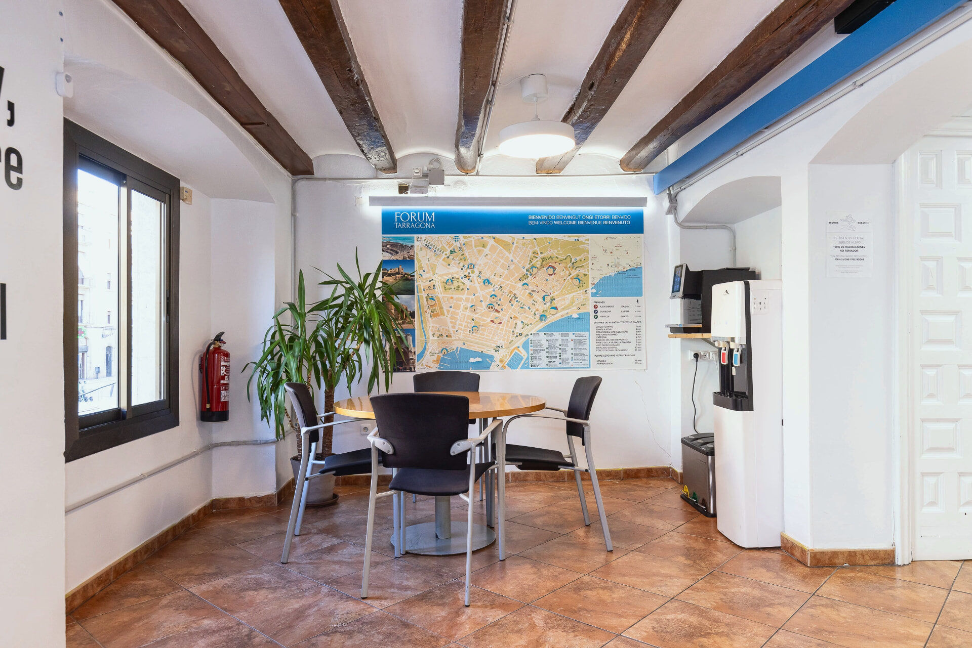 Mesa con sillas y mapa de Tarragona en la sala común, junto a las ventanas a la plaza.