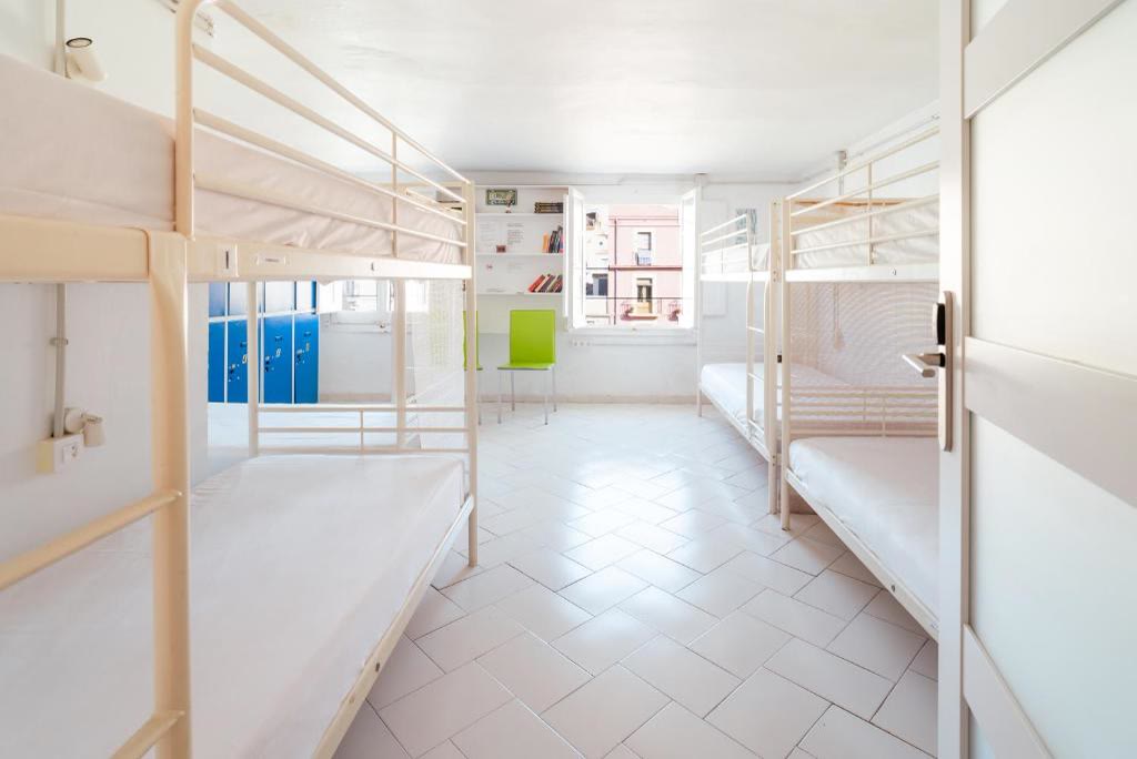 Dormitorio compartido de 8 camas, luminoso, con literas blancas y taquillas azules.